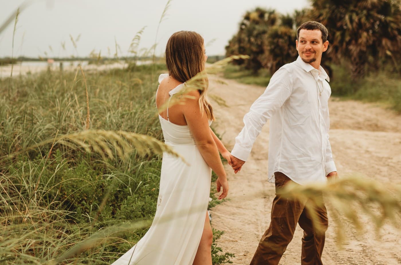 Heather and William walking hand in hand along a sandy path through beach grass